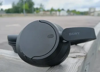 Schwarze Sony WH-CH720N auf einem Holzgeländer mit Parkplätzen im Hintergrund