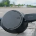 Schwarze Sony WH-CH720N auf einem Holzgeländer mit Parkplätzen im Hintergrund