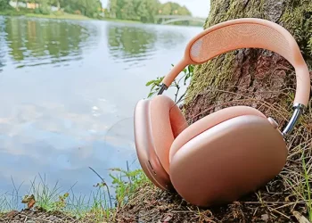 Apple AirPods Max 2 Orange an einen Baumstamm gelehnt mit einem Bach im Hintergrund