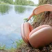 Apple AirPods Max 2 Orange an einen Baumstamm gelehnt mit einem Bach im Hintergrund