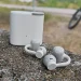 Hellgraue CMF Clip Pro mit dem Ladecase im Hintergrund auf einer grauen Betonbarriere